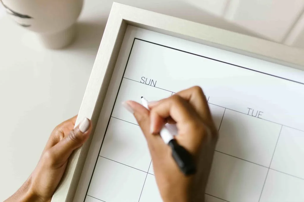 Mano apuntando fechas en un calendario semanal